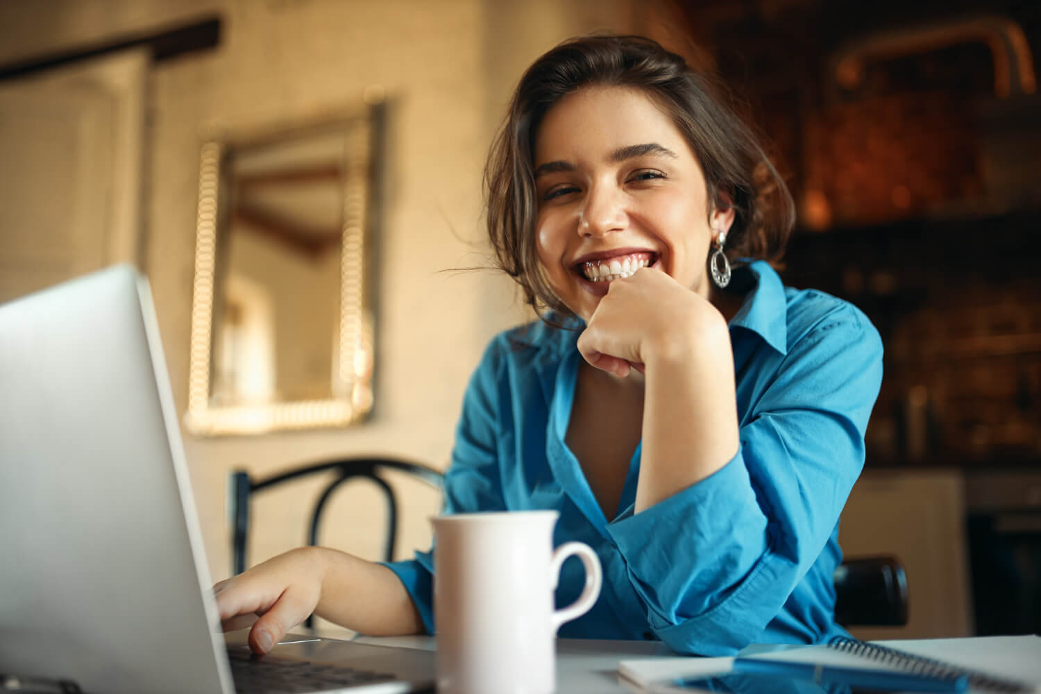 Mulher sorrindo radiante enquanto trabalha no notebook. Saiba como é a rotina após um implante dentário em São Bento do Sul.